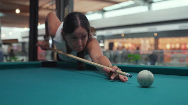 Focused woman playing billiards hitting cue ball