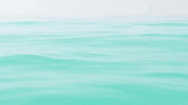 Calm turquoise ocean surface with gentle waves under a hazy sky