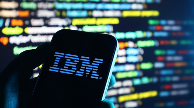 IBM logo on smartphone screen with blurred programming code background.