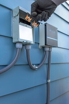 Side view of electrician hand removing a pullout switch disconnect from an outdoor AC disconnect box near a surge protector on a blue siding house wall