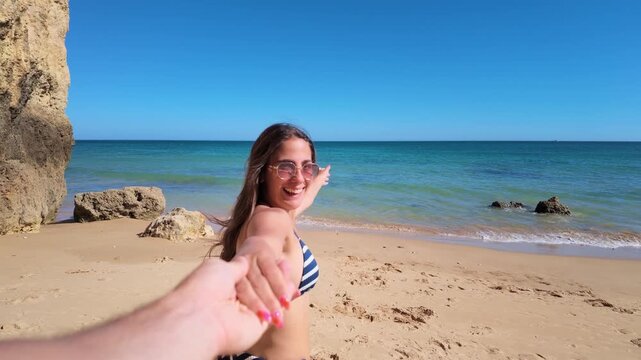 Young woman in a bikini holding hands with her partner and running towards the sea