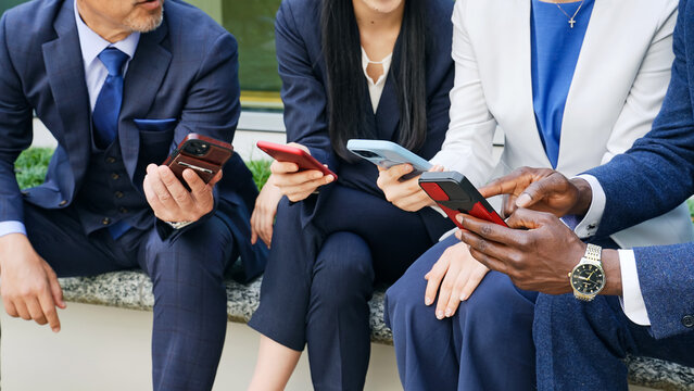 屋外ベンチでスマホを見る多国籍ビジネスパーソンのグループ