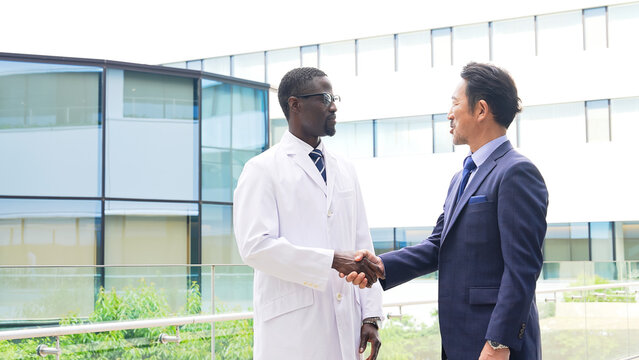 A foreign man in a white coat shaking hands with a businessman.