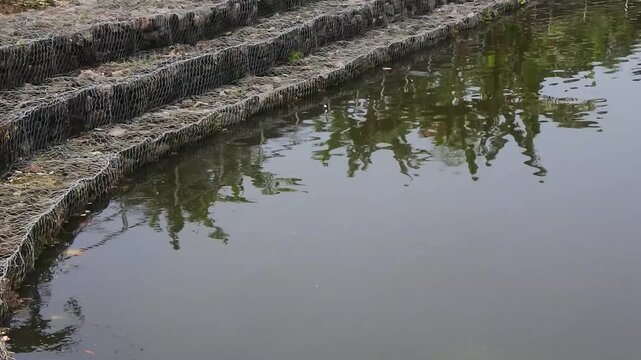 The multi tiered gabion retaining wall with wire cage filled with rocks in a mini dam