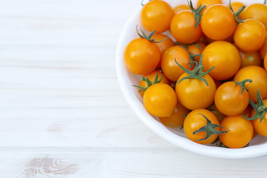 Full white ceramic bowl of bright orange cherry tomatoes, Sungold variety, on the white wooden rustic table.