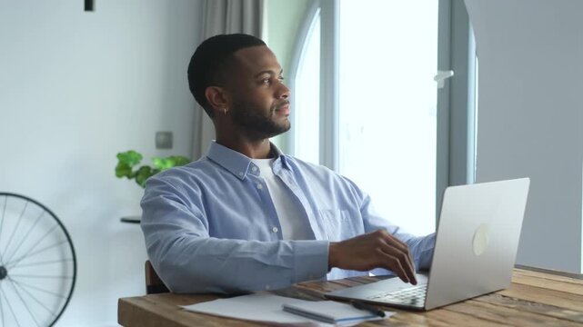 Relaxed male freelancer finishing work on his laptop, stretching his arms, and leaning back with satisfaction