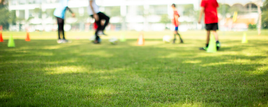 Selective focus to grass on a football field with blurry the Kid football players are training with the coach.