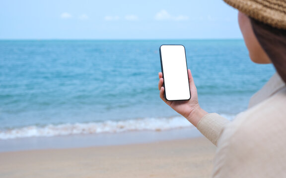 Mockup image of a woman holding mobile phone with blank desktop screen by the sea