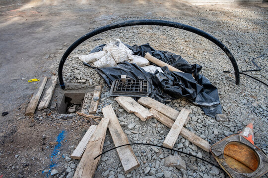 Old open meter shut-off box on job site for home rebuild, sandbags, lumber, plastic tarp, conduit, and other debris in a trash pile, new housing build
