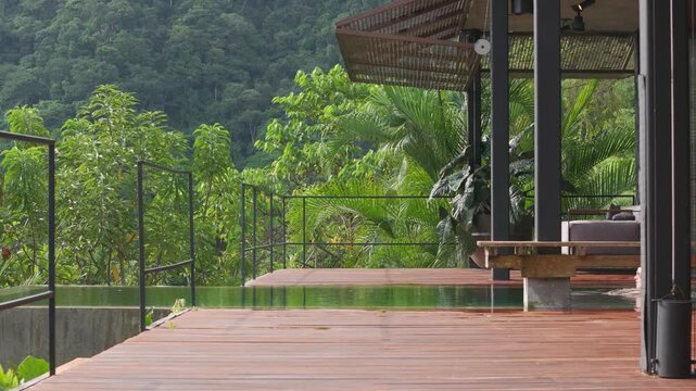 Girl swimming in pool at luxurious villa surrounded by lush tropical rainforest and mountains. Modern wooden deck terrace with elegant outdoor furniture creates serene paradise retreat setting.