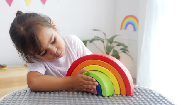Kid playing with rainbow wood toy at preschool classroom. Kindergarten learning games for children at nursery