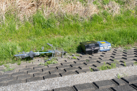 河原の土手に捨てられた不法投棄された旅行ケースと自転車