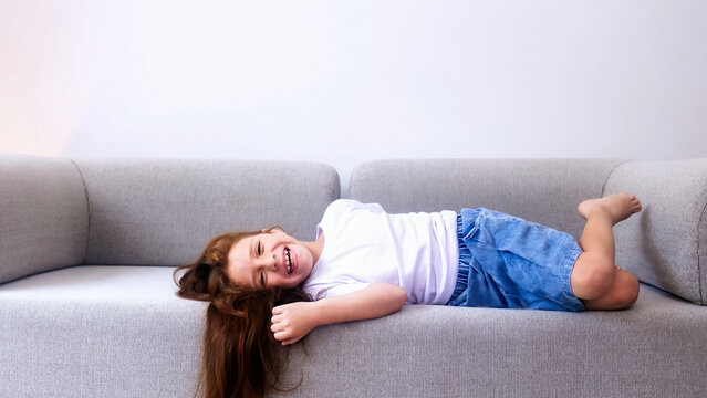 Happy little girl having fun lying on couch at home - Focus on child face 