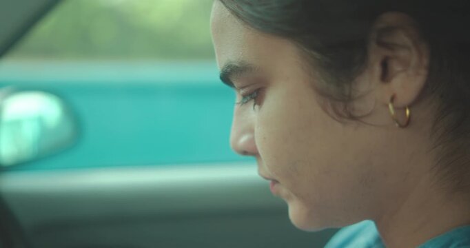 A playful boy pulls silly faces in the backseat while a young woman drives ahead.