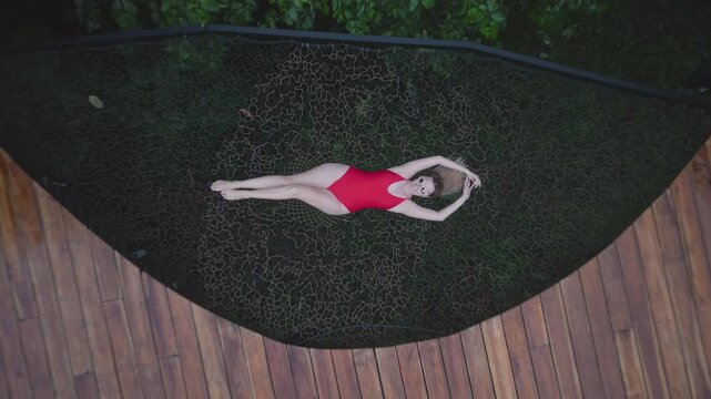 Aerial drone footage ascending over luxury eco-resort featuring white geodesic dome structures connected by curved wooden decks, woman relaxing on trampoline in red swimsuit.