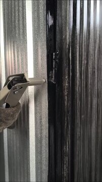 Hands with protective gloves using a riveting tool on a galvanized iron wall panel