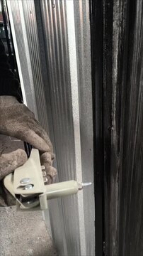 Close up of a worker using a hand rivet gun on a corrugated metal sheet, vertical video