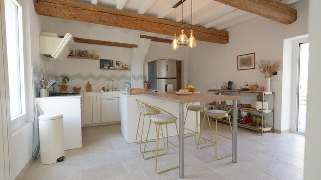 a beautiful, bright and modern kitchen with beige flooring, white walls, white and wooden worktops, a ceiling featuring two large exposed wooden beams, a three-bulb light fitting and high chairs