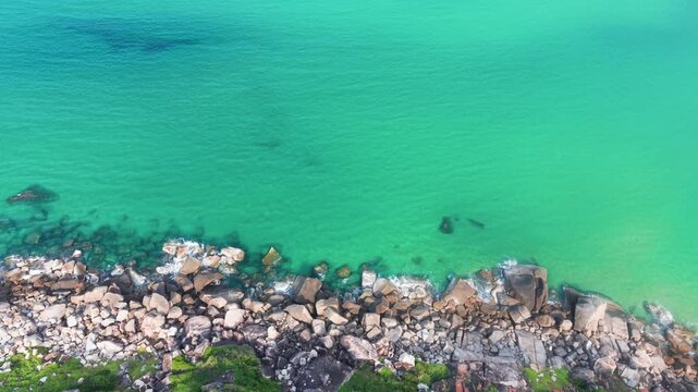 Footage shows the clear blue water meeting rocky shores in Dak Lak, Vietnam. Nature reveals its beauty with each wave crashing on the rocks. The vibrant colors attract viewers to explore.
