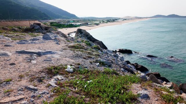 Views of the coastline in Dak Lak, Vietnam show rocks, water, and land. The sun sets over the ocean. Waves crash against the shore. Nature and landscape are highlighted during this quiet time.