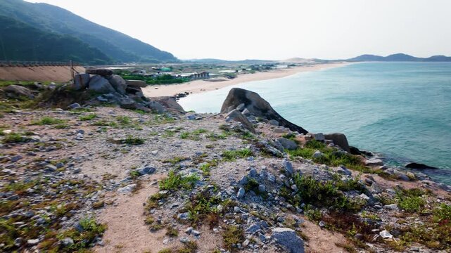 Waves crash on the shore as the camera looks out over the coastline of Dak Lak. The rocky landscape meets the sea under a clear sky.