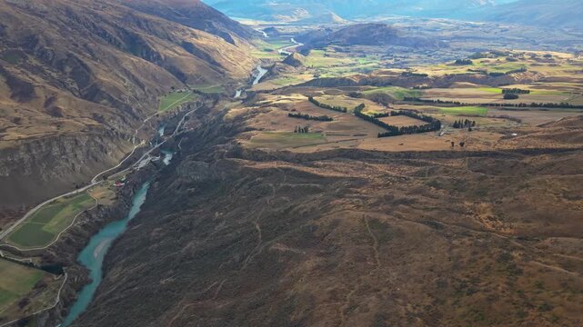 Aerial view of winding Crown Range Road and river through alpine valley farmland
