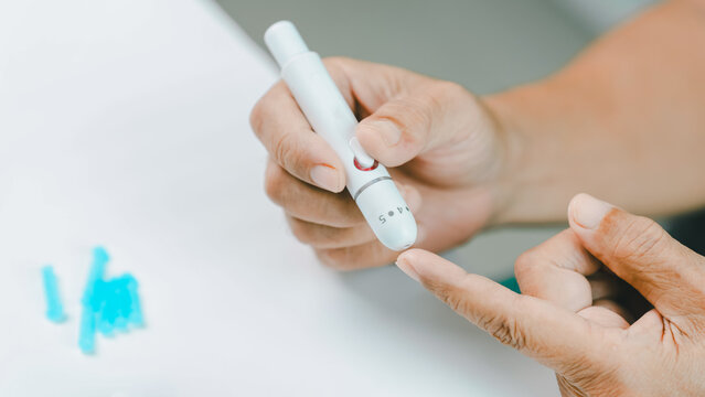 Close-up of a senior adult preparing a finger prick with a lancet device for blood glucose testing at home. Diabetes self-monitoring promotes preventive healthcare, chronic disease management.