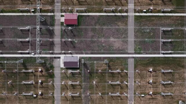 An overhead drone view shows an organized electrical substation with transmission lines and industrial equipment arranged in a precise grid.