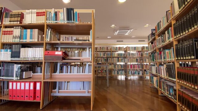 Empty library interior featuring multiple aisles of tall bookshelves filled with various books and reading tables with chairs