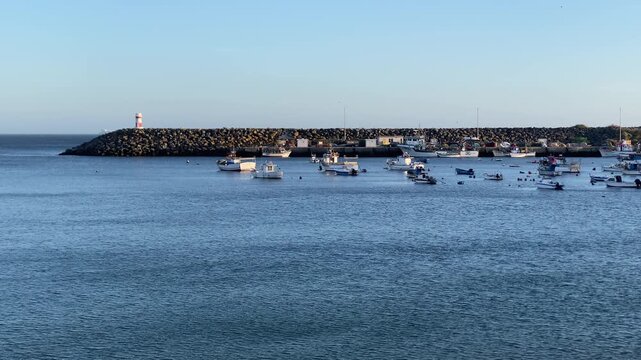 Sailboats moving into a port with a protective breakwater and lighthouse, offering an outlook on maritime industry
