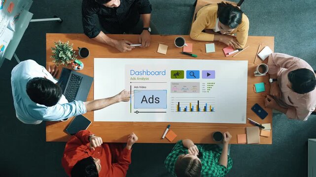 Collaborative Meeting Around Dashboard Displaying Advertising Analysis with Charts and Data Insights on a Wooden Table in an Office Setting Gluon.