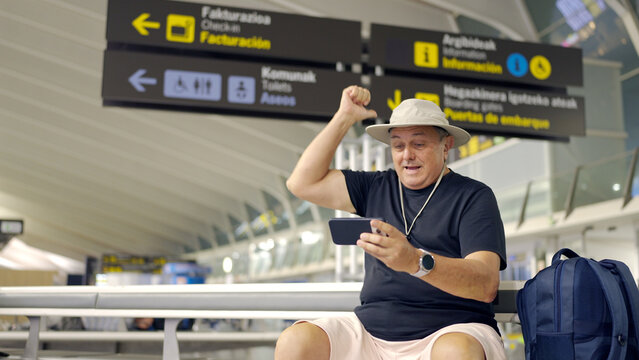 Man celebrating win on smartphone in airport terminal