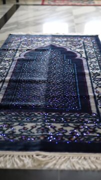 Islamic prayer rug with intricate blue floral pattern and sparkling embellishments on marble floor, religious textile