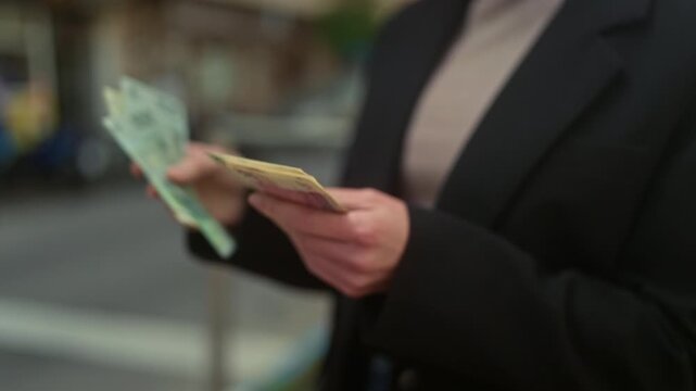 Woman counting banknotes with hands on street while holding a small stack of cash checking denominations; concentration finance.