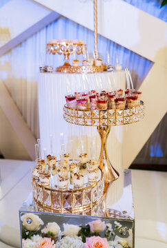 Mesa de postres elegante con copas de postre, bandejas doradas y decoraci&oacute;n floral para boda o evento