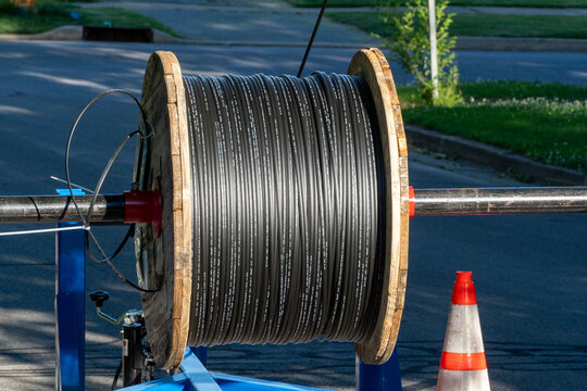 Large wooden spool of new black fiber optic cable ready for installation on a street, vital for high-speed internet, data, and modern telecommunication infrastructure deployment.