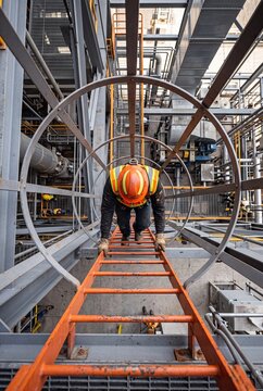 Construction Worker Climbing Safety Ladder in Industrial Environmentv