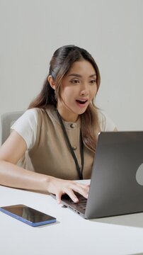Beautiful young Asian woman is typing report on her laptop while feeling happy.