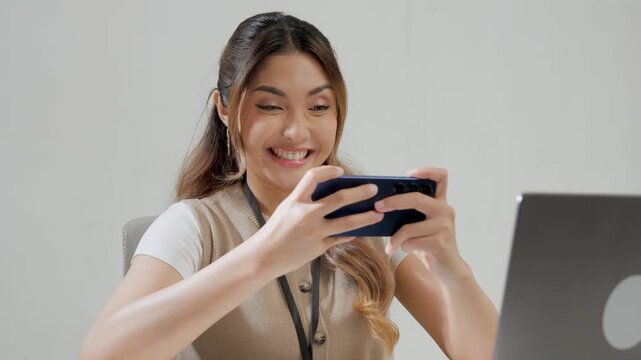 Joyful young Asian woman is watching streaming video or playing game on her smartphone.