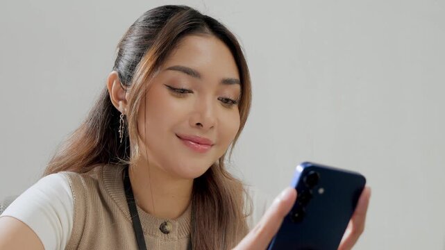 Cheerful young Asian woman is working while using smartphone to text someone or open social media.