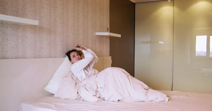 Morning routine. Home comfort. Calm woman relaxing in bed under beige blanket enjoying peaceful everyday atmosphere cozy interior.