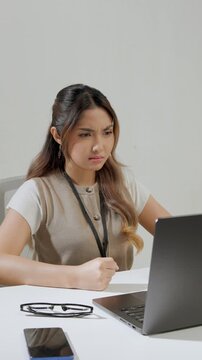 Angry young Asian female employee is feeling frustrated at work and slamming her desk.