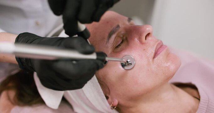 Facial procedure. Beauty lifting. Woman cosmetician in black gloves using professional device for microcurrent skin rejuvenation.