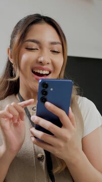 Happy young Asian woman is working while using smartphone to text someone or open social media.