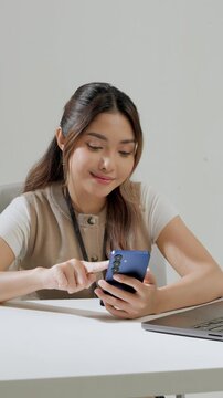 Happy young Asian woman is working while using smartphone to text someone or open social media.