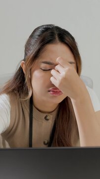 Young Asian female employee is working using her laptop while feeling headache and stressful.