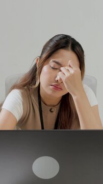 Young Asian female employee is working using her laptop while feeling headache and stressful.