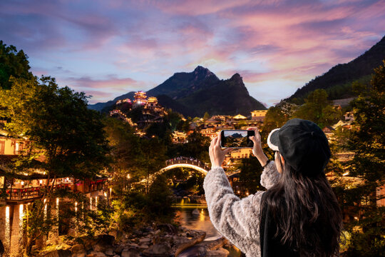 Young female tourist using smartphone to take photo of the beautiful view of Wangxian Valley decorated with beautiful lighting at Shangrao, China