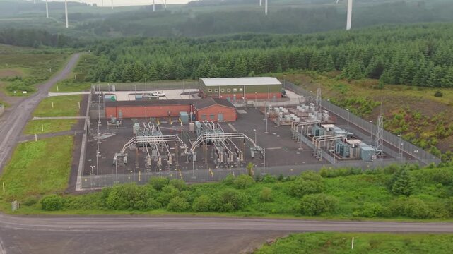 Electrical Substation Managing and Re-Directing Flow of Electricity on Natural Landscape with Wind Turbines in Background.