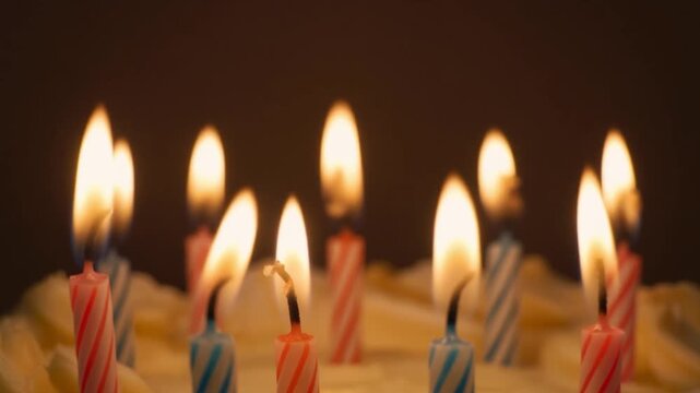 Burning birthday candles on delicious cake with flickering flames close up macro view celebration background